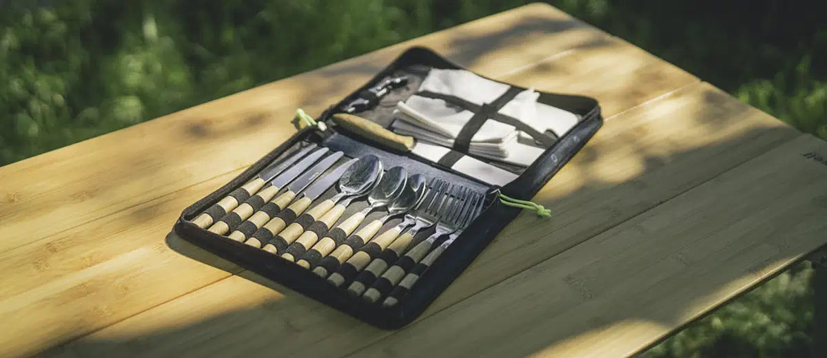 Outwell Morella Picnic Cutlery Set with stainless steel forks, knives, and spoons on a wooden table for outdoor dining.